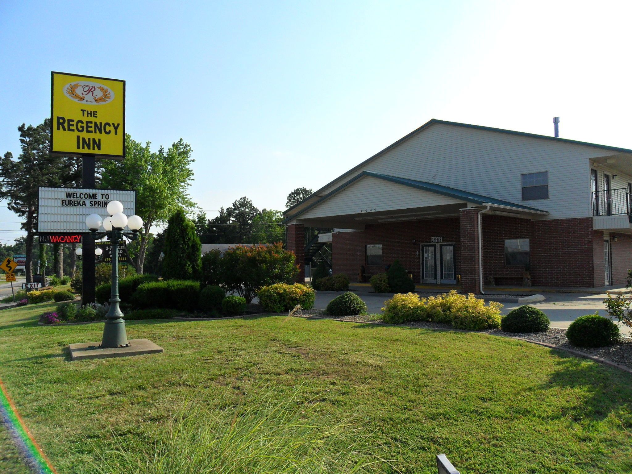 A two-story building with a brick facade and a flat roof. There is a sign in front indicating 'The Regency Inn' and 'Welcome to Eureka Springs'.