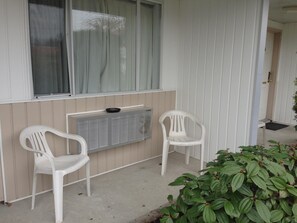 A small porch with two white plastic chairs, a radiator, and a window with curtains.