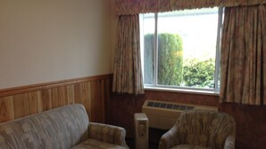 A room with a wooden paneled wall, a sofa, a chair, and a window with curtains.
