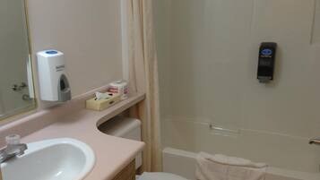 A bathroom with a sink, toilet, and shower. There are toilet paper and a hand dryer on the wall.