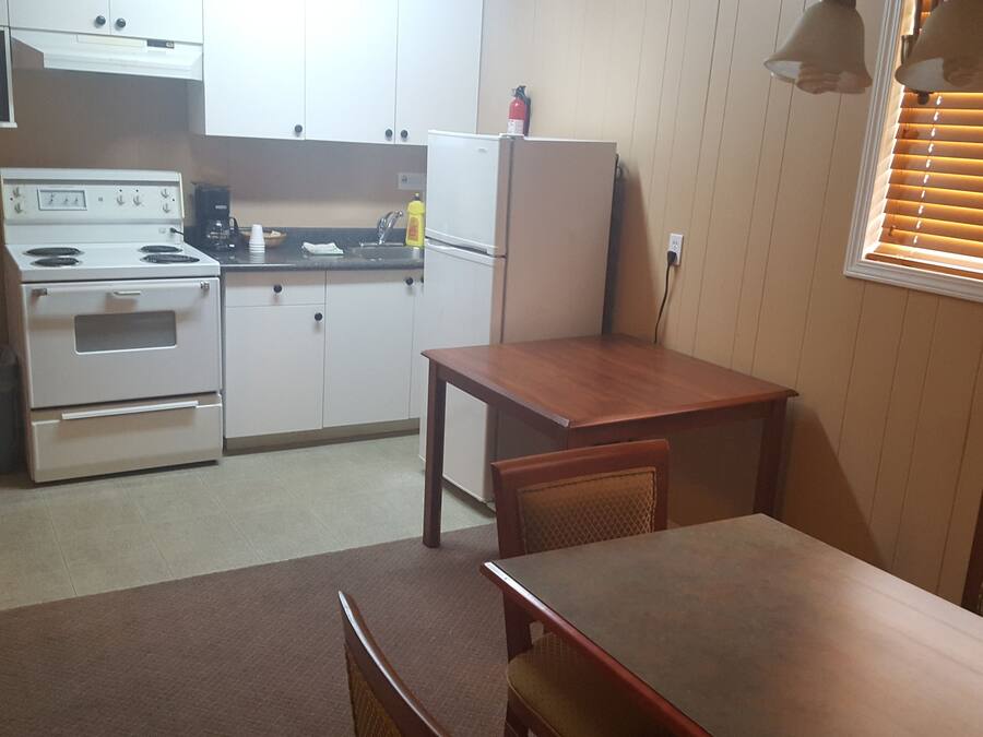 Una cocina compacta con electrodomésticos blancos, una mesa de madera y una ventana con persianas.