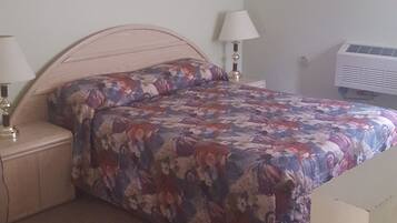A bedroom with a floral bedspread, two bedside lamps, a white air conditioner, and a wooden nightstand.