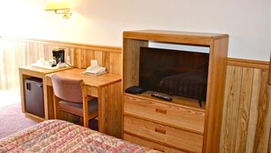 A hotel room with a wooden desk, a chair, a bed, a TV, a lamp, a coffee maker, and a phone.