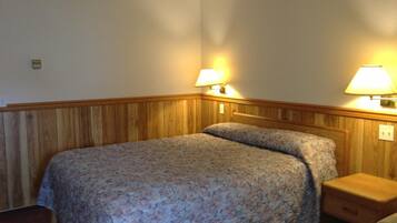 A single bed with a floral bedspread in a room with wooden paneling on the walls and a nightstand with a lamp.