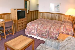 A small, cozy room with a bed, a desk, a chair, a TV, and a lamp.