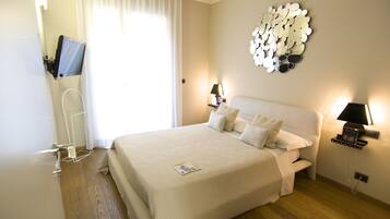 Een hotelkamer met een groot bed, een flatscreen televisie aan de muur, een nachtkastje met een lamp en een decoratieve spiegel.