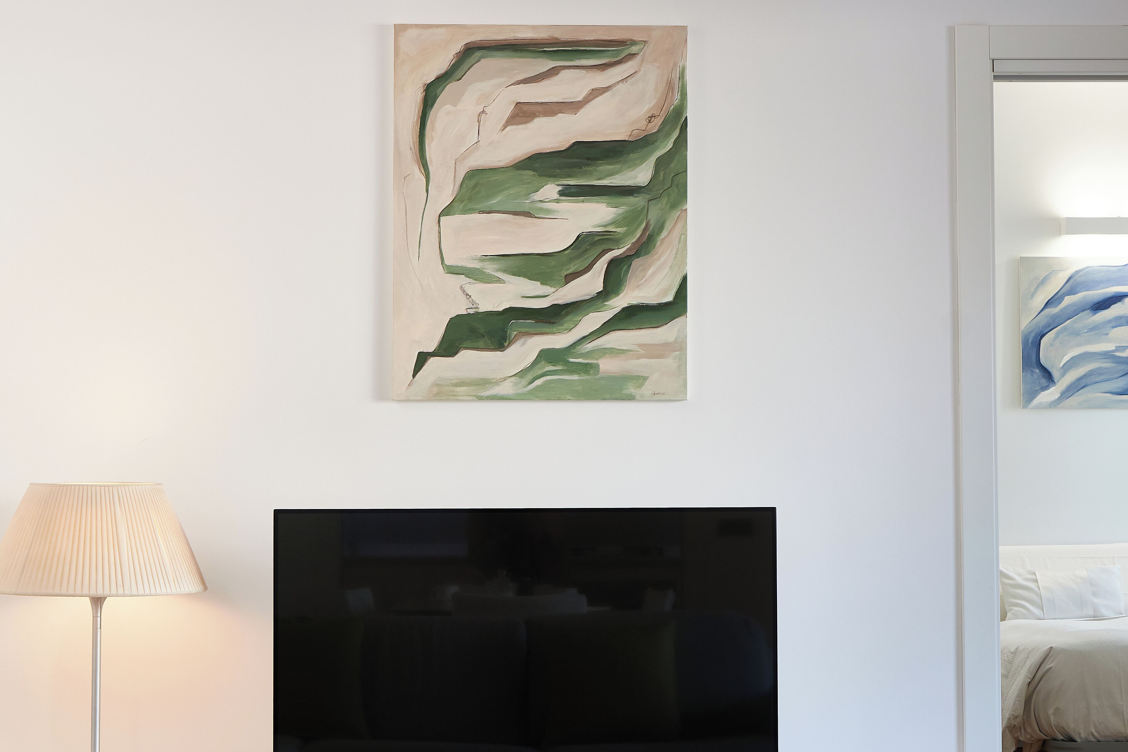 Uma sala de estar moderna com televisão de tela plana, uma luminária e arte abstrata na parede.