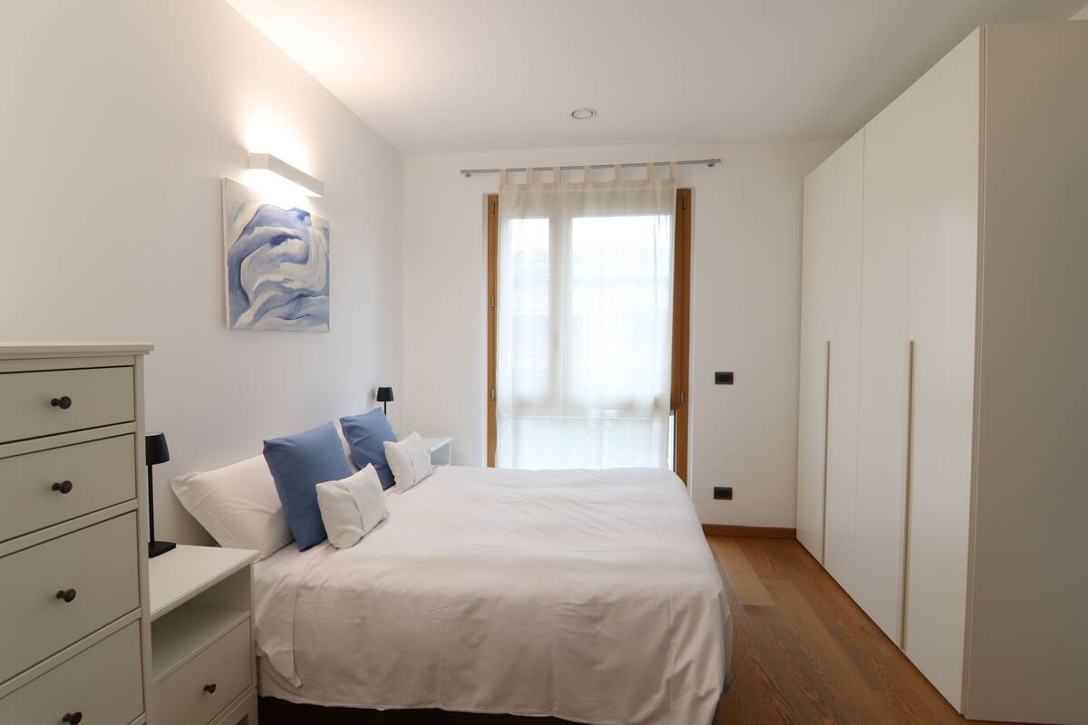 A bedroom with a bed, a dresser, a painting, and a window with curtains.