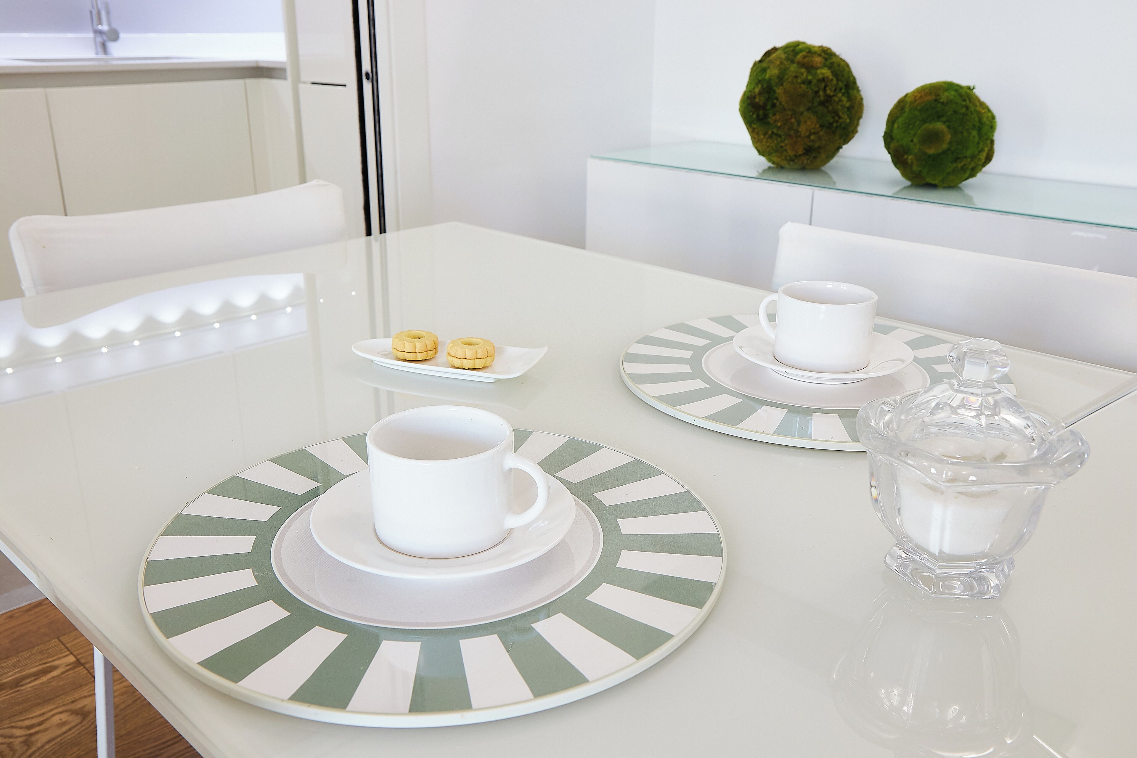 Ein weißer Tisch mit einer Glasplatte, zwei weiße Tassen, zwei Untertassen und eine kleine Glas Karaffe.