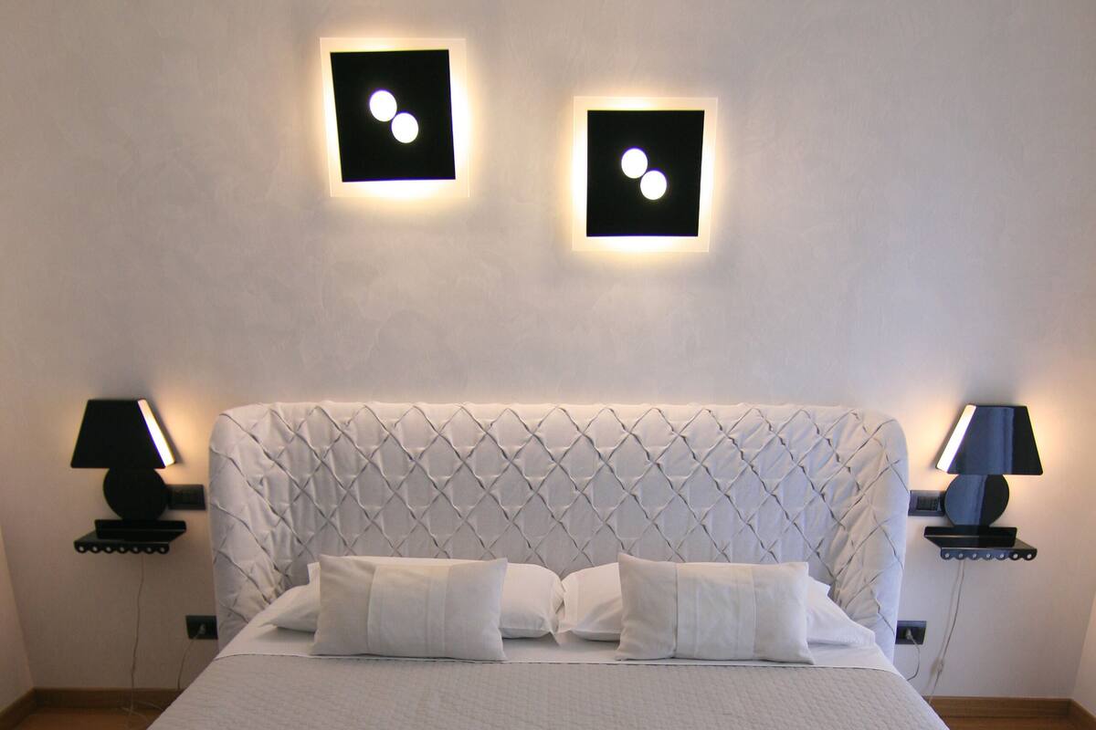 A neatly made bed with a quilted headboard, two bedside lamps, and rose petals on the bed.