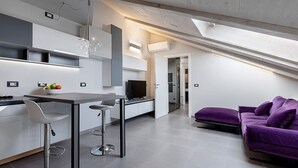A modern kitchen with a dining area, a purple sofa, and a TV. - Experience Design Bed & Show (Milan)