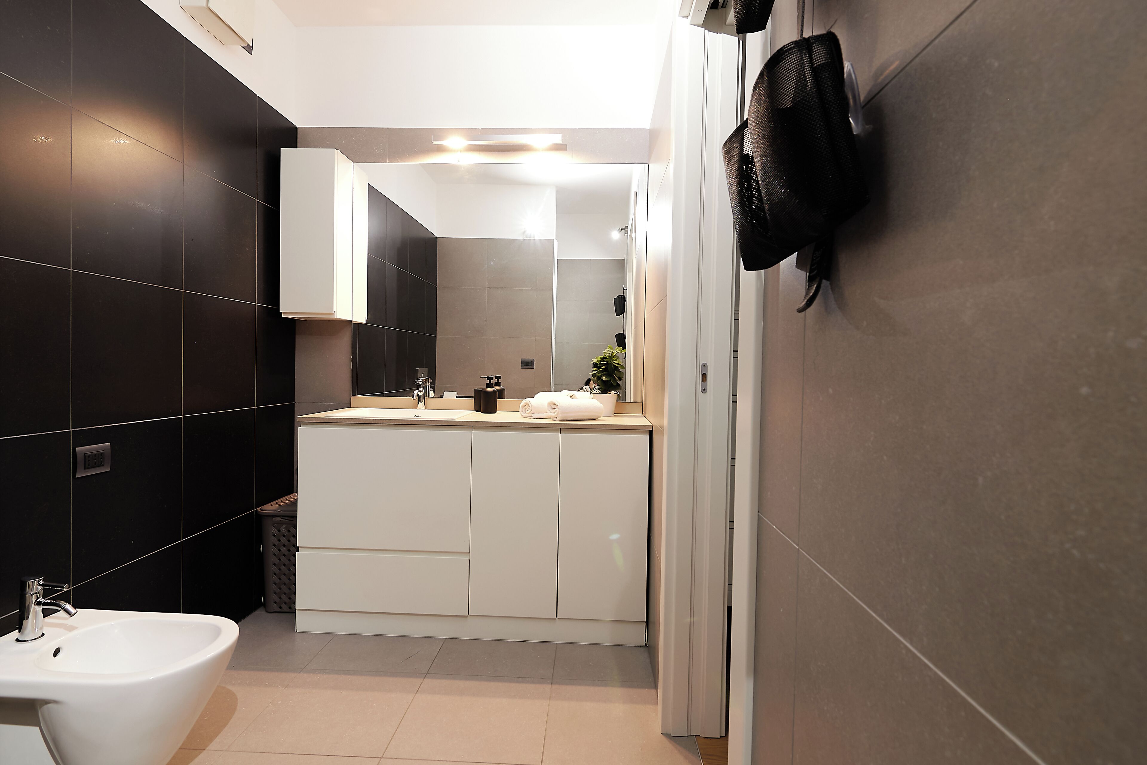 A modern bathroom with a white sink, dark tiled walls, and a glass shower enclosure.