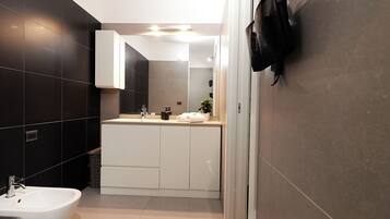 A modern bathroom with a white sink, dark tiled walls, and a glass shower enclosure.