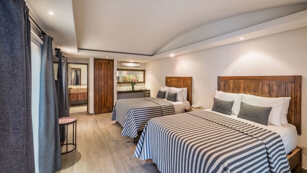 Quarto de hotel com duas camas, um espaço para sentar pequeno e um banheiro visível através de uma porta aberta.
