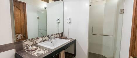 Un baño con lavamanos blanco, un espejo, toallero y cabina de ducha de vidrio.
