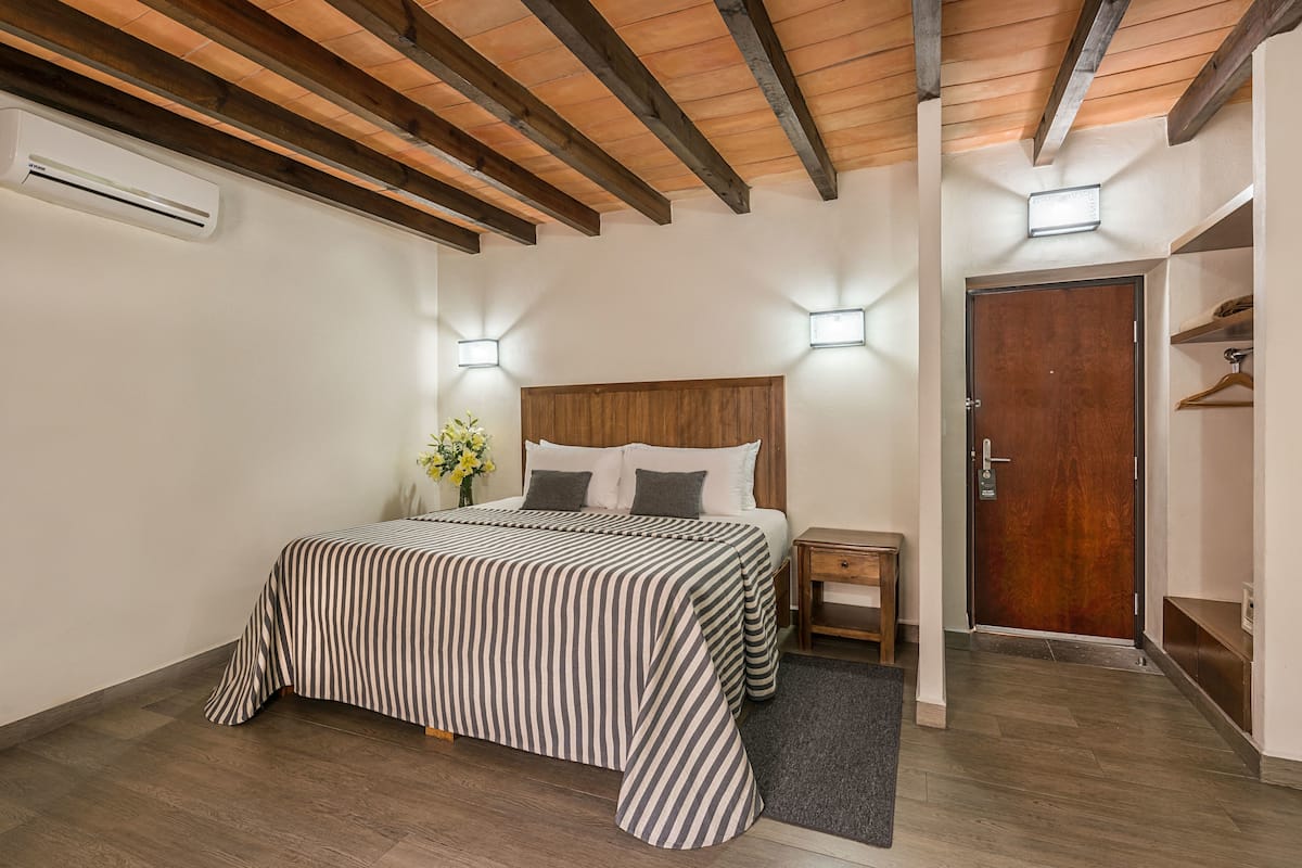 Un dormitorio con techo de madera, una cama con ropa de cama a rayas, lámparas de noche y una puerta que da a un armario.