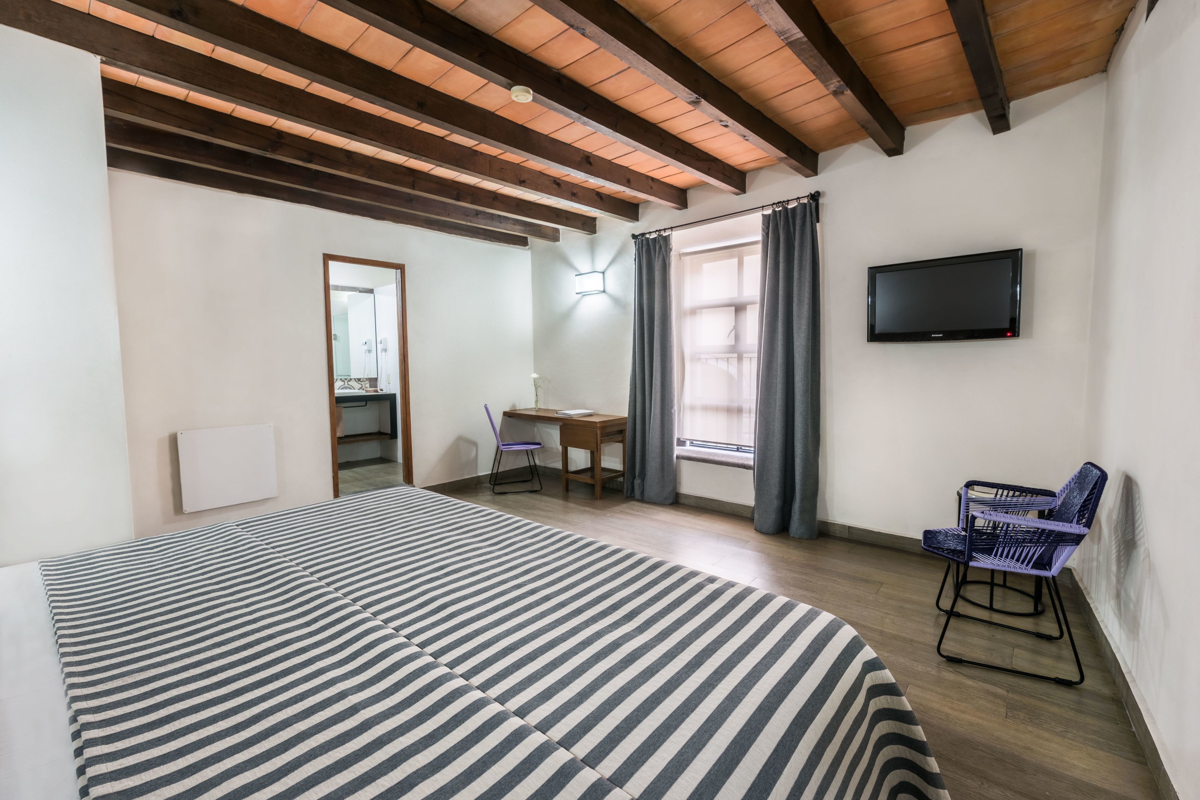 A hotel room with a large bed, a desk with a chair, a television, and a window with curtains.
