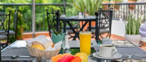 Una mesa con una fuente de fruta, un vaso de jugo de naranja, una taza de café y una cesta de pan.