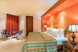 Habitación de hotel con una cama, dos sillas, una mesita, una mesita de noche y una lámpara.