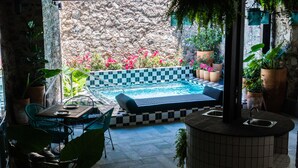 Uma área de piscina com piso xadrez, espreguiçadeiras e plantas em vasos.