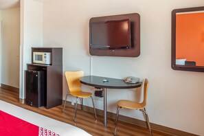A hotel room with a bed, a small desk with a telephone, two chairs, a microwave, and a television mounted on the wall.
