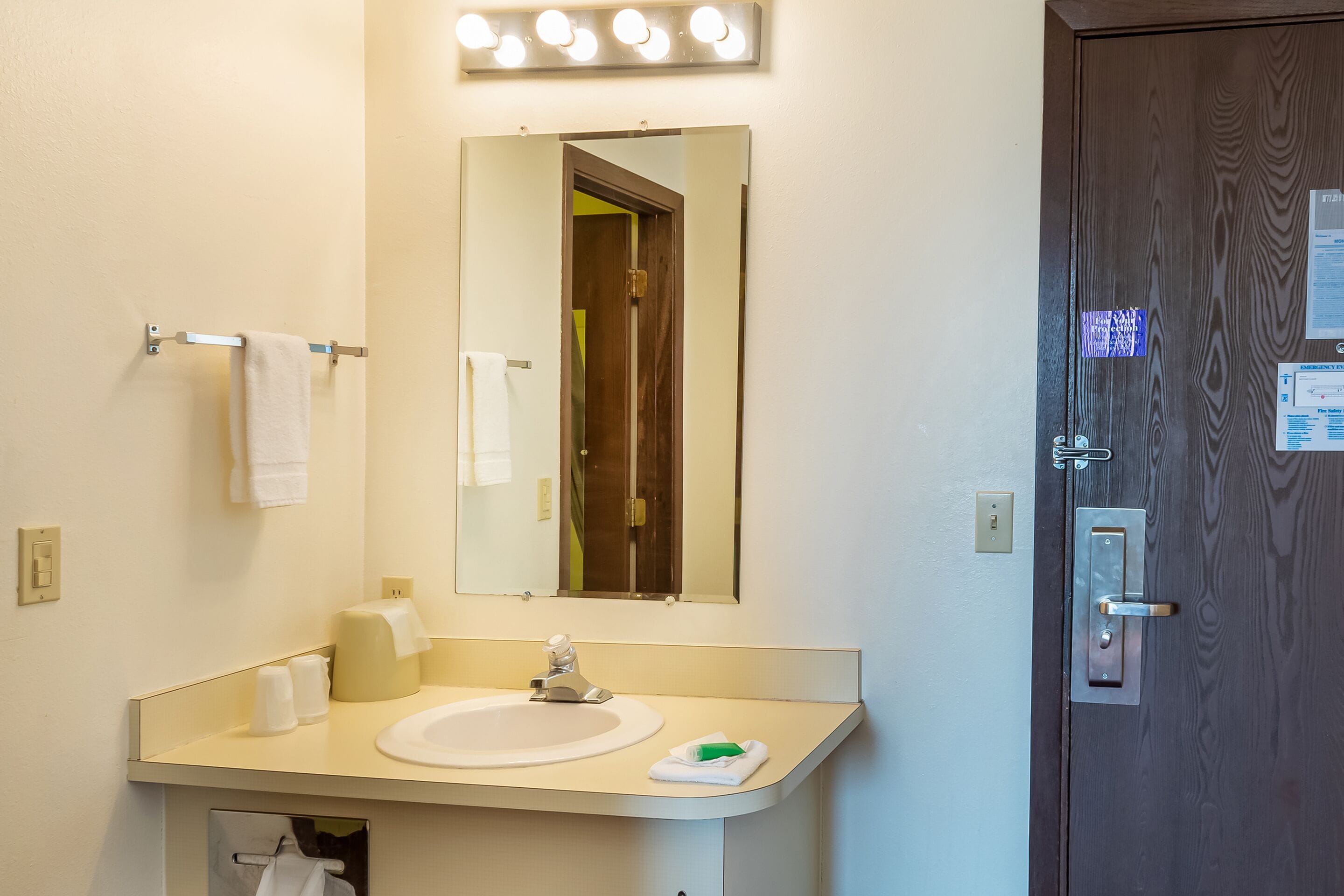A hotel bathroom with a sink, mirror, and towel rack.