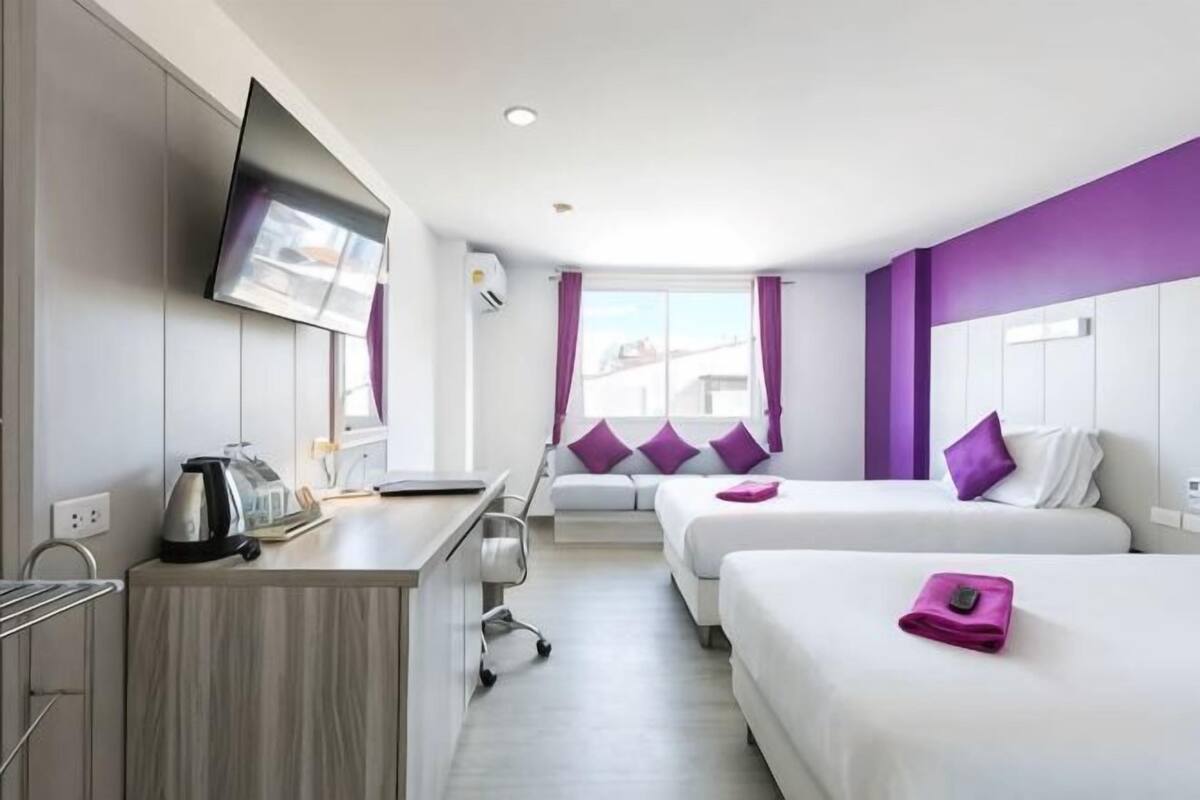Habitación de hotel con dos camas, un escritorio, un televisor y una ventana con cortinas.
