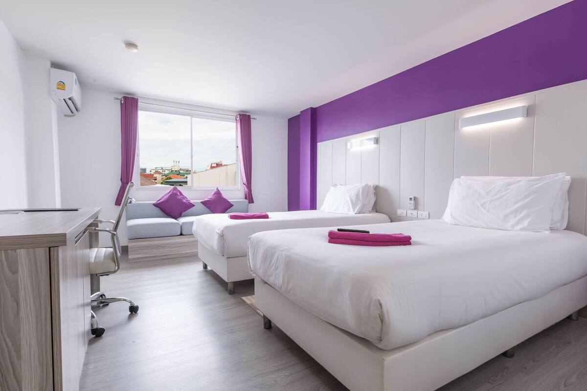 Habitación de hotel con dos camas, un escritorio y una ventana con cortinas moradas.