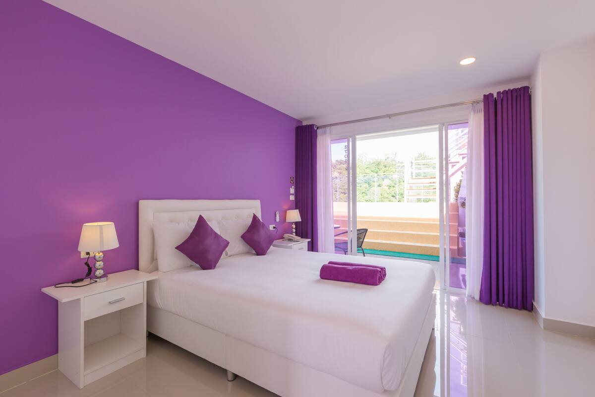 Habitación de hotel con una cama grande, cortinas moradas y vistas al exterior.