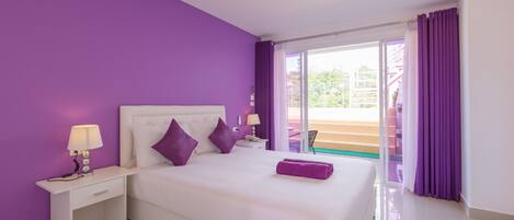 A hotel room with a large bed, purple curtains, and a view of the outside.