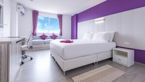 A modern bedroom with a white bed, purple accents, a desk, and a window with curtains. - Hotel Zing (Pattaya)