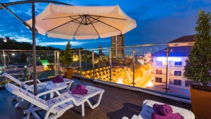 A rooftop terrace with white lounge chairs and a large umbrella, overlooking a cityscape at dusk. - Hotel Zing (Pattaya)