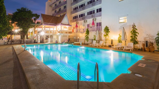 A swimming pool with lounge chairs and umbrellas, surrounded by a building with balconies and a covered area. - Hotel Zing (Pattaya)
