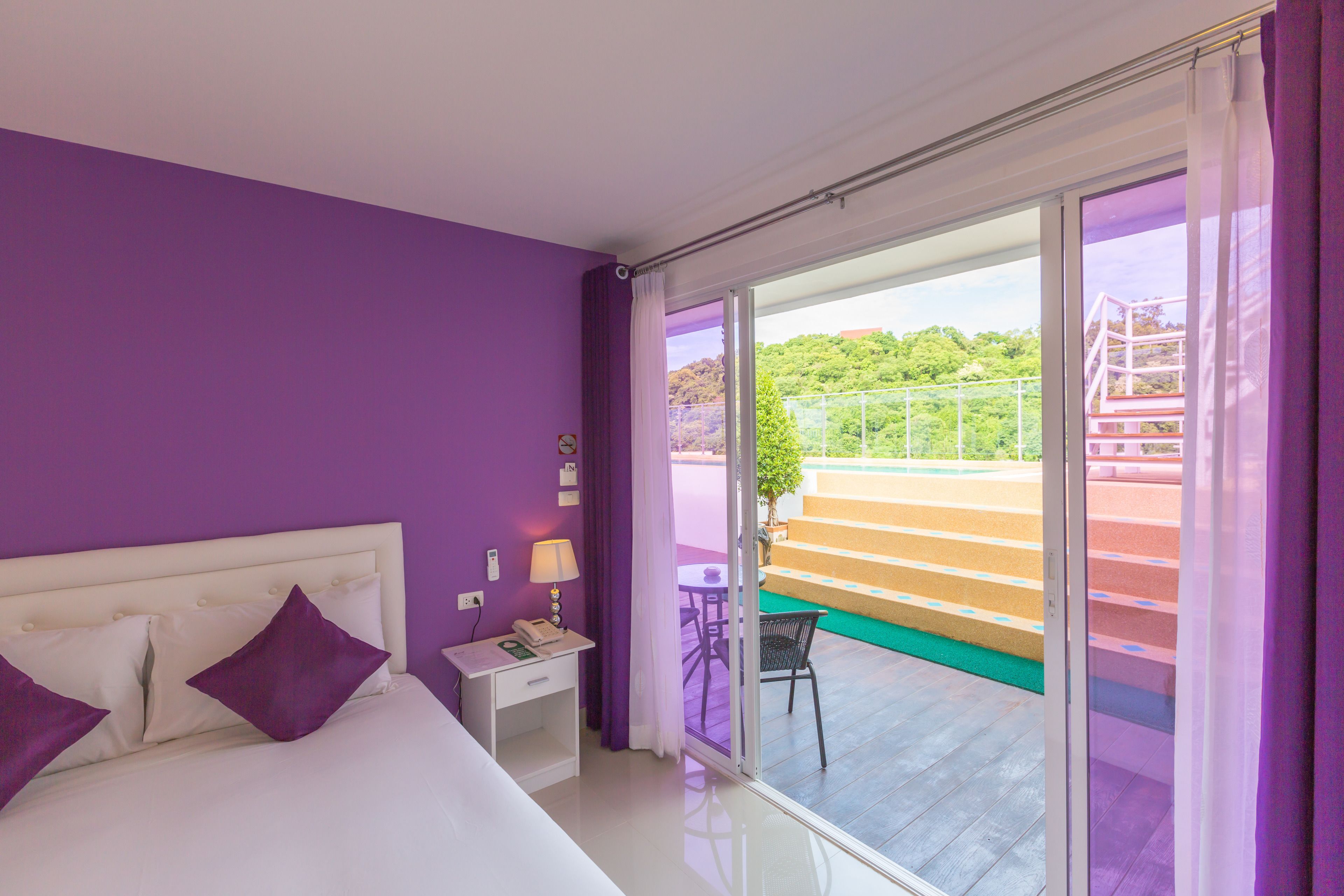 A bedroom with a bed, nightstand, and a view of a balcony with outdoor furniture.