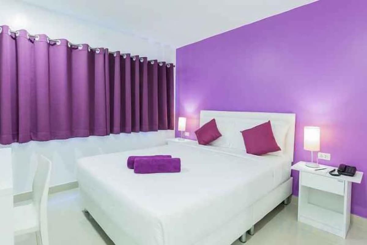 A hotel room with a bed, a nightstand, a chair, and purple curtains.