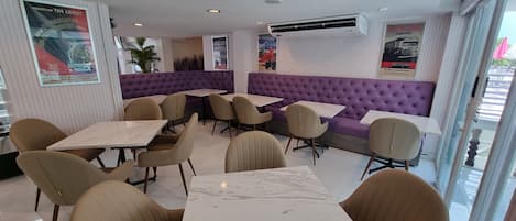 A restaurant with purple booths and beige chairs, marble tables, and posters on the walls.