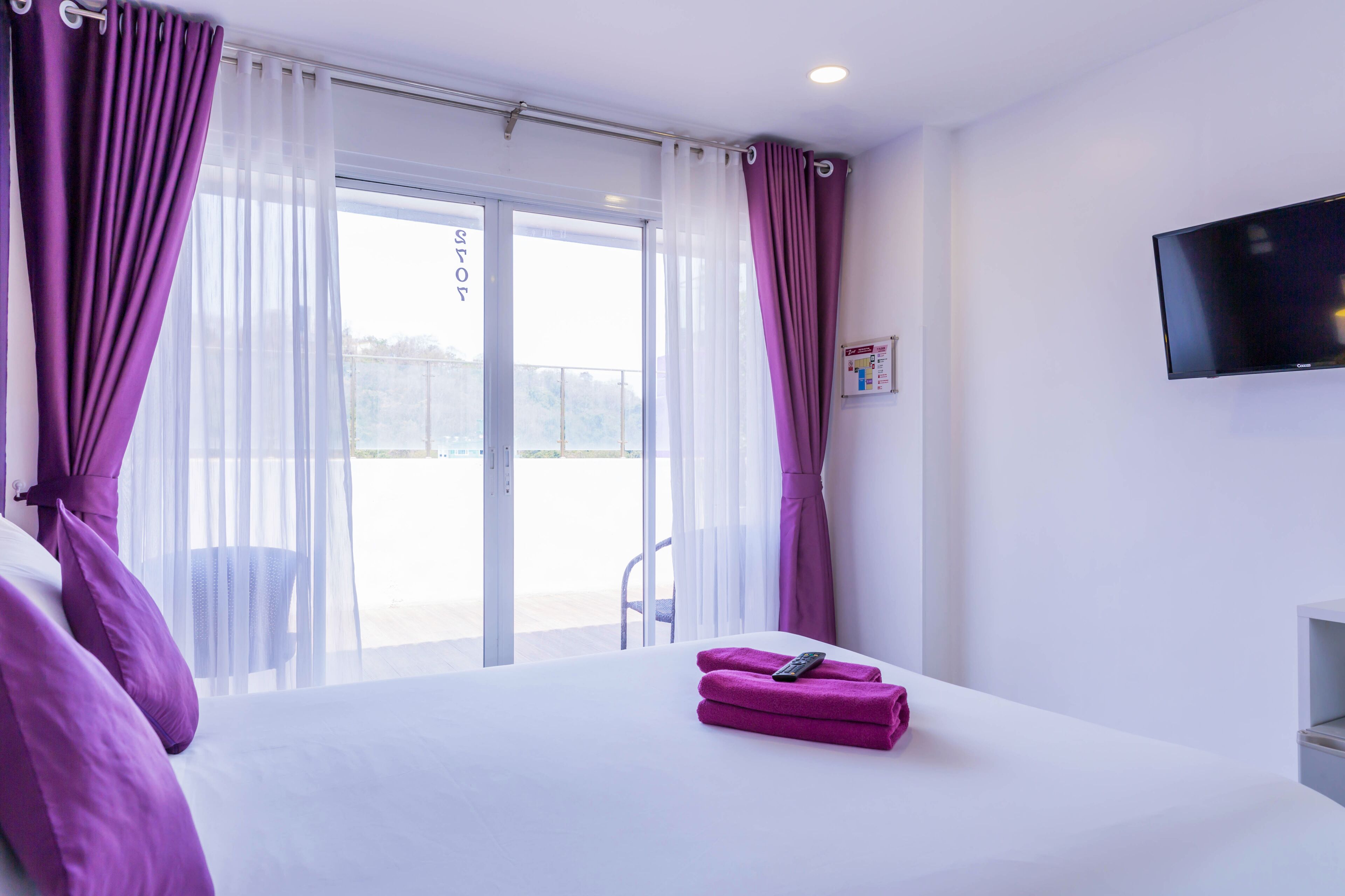 Een hotelkamer met een bed, een aan de muur bevestigde televisie en een balkon met een stoel.