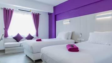 A hotel room with two beds, a sofa, purple curtains, and a window with an air conditioning unit.