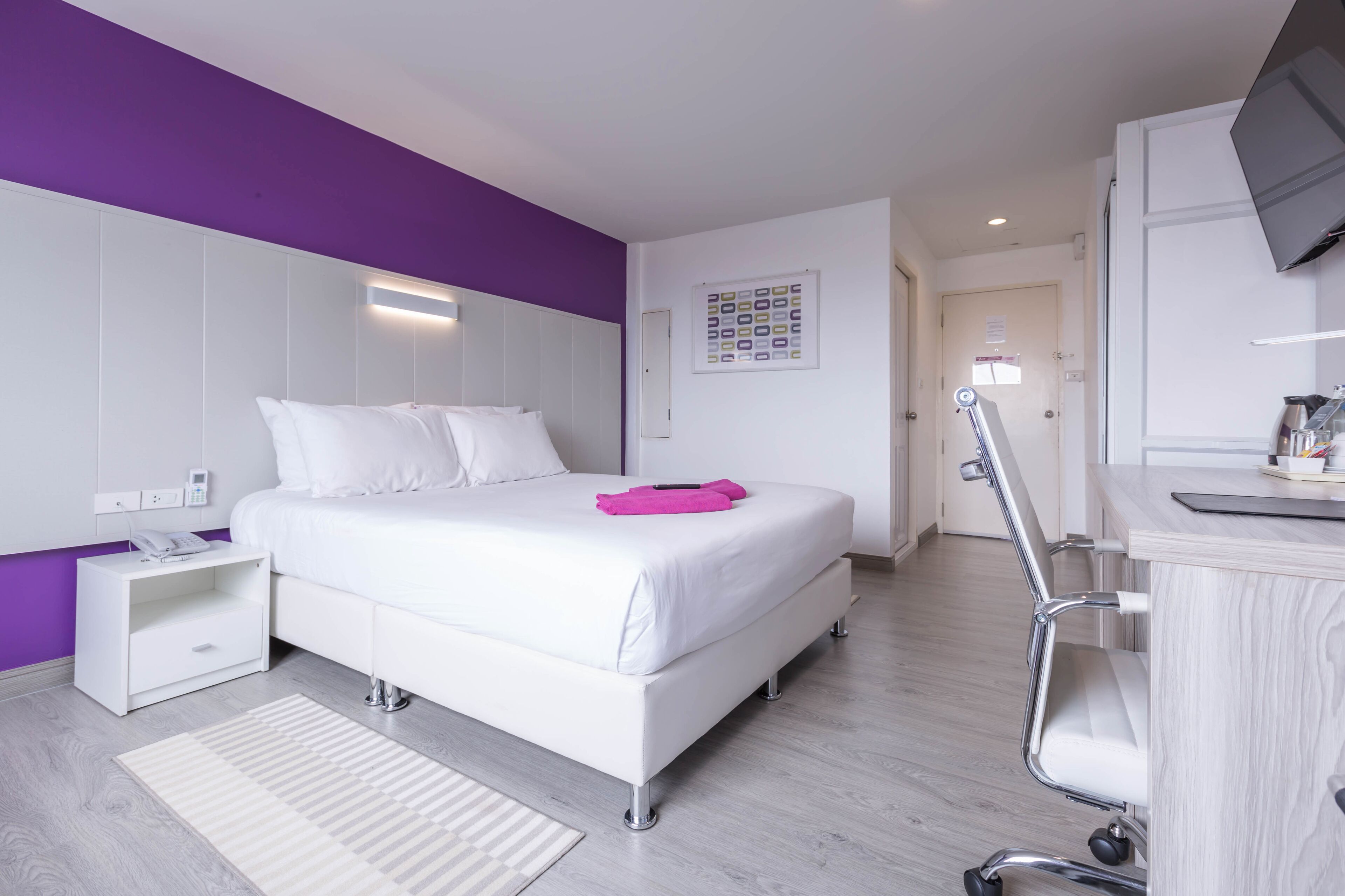A modern hotel room with a large bed, a desk, and a chair.