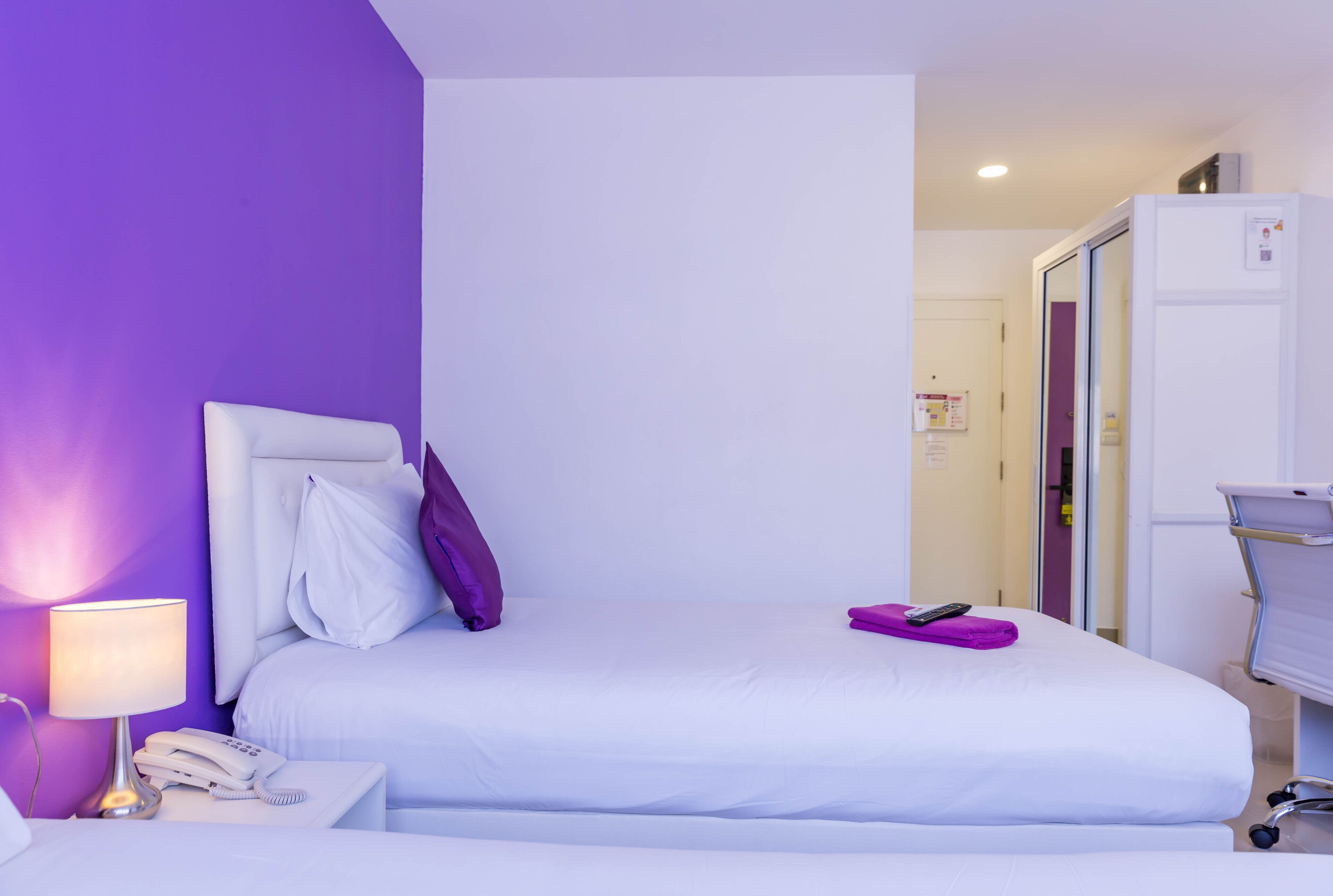 Habitación de hotel con una cama, una mesita de noche con lámpara y teléfono, y un baño visible a través de una puerta abierta.