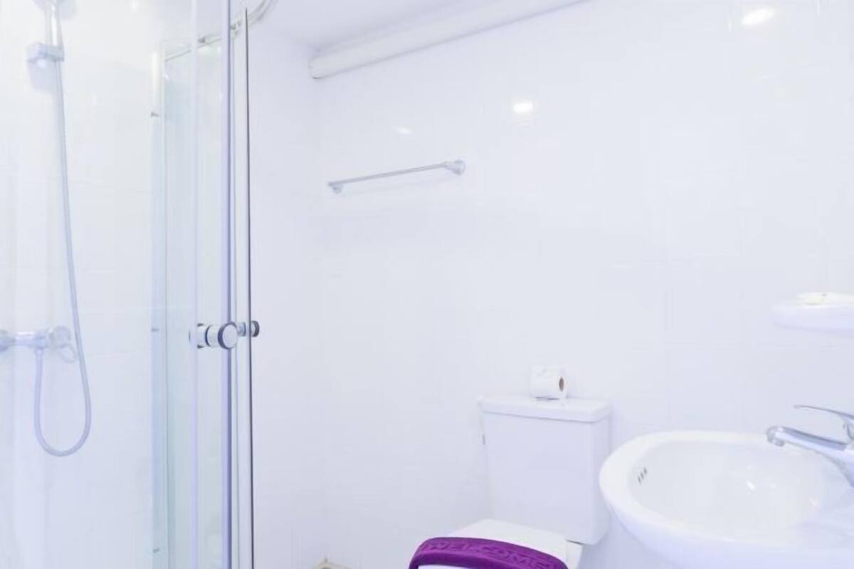 Un baño con cabina de ducha de vidrio, inodoro y lavamanos blancos.