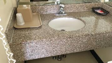 Un baño con encimera de granito, lavabo, espejo y dispensador de toallas.