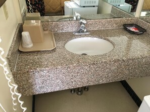 Baño con encimera de granito, lavamanos blanco, espejo y dispensador de toallas.