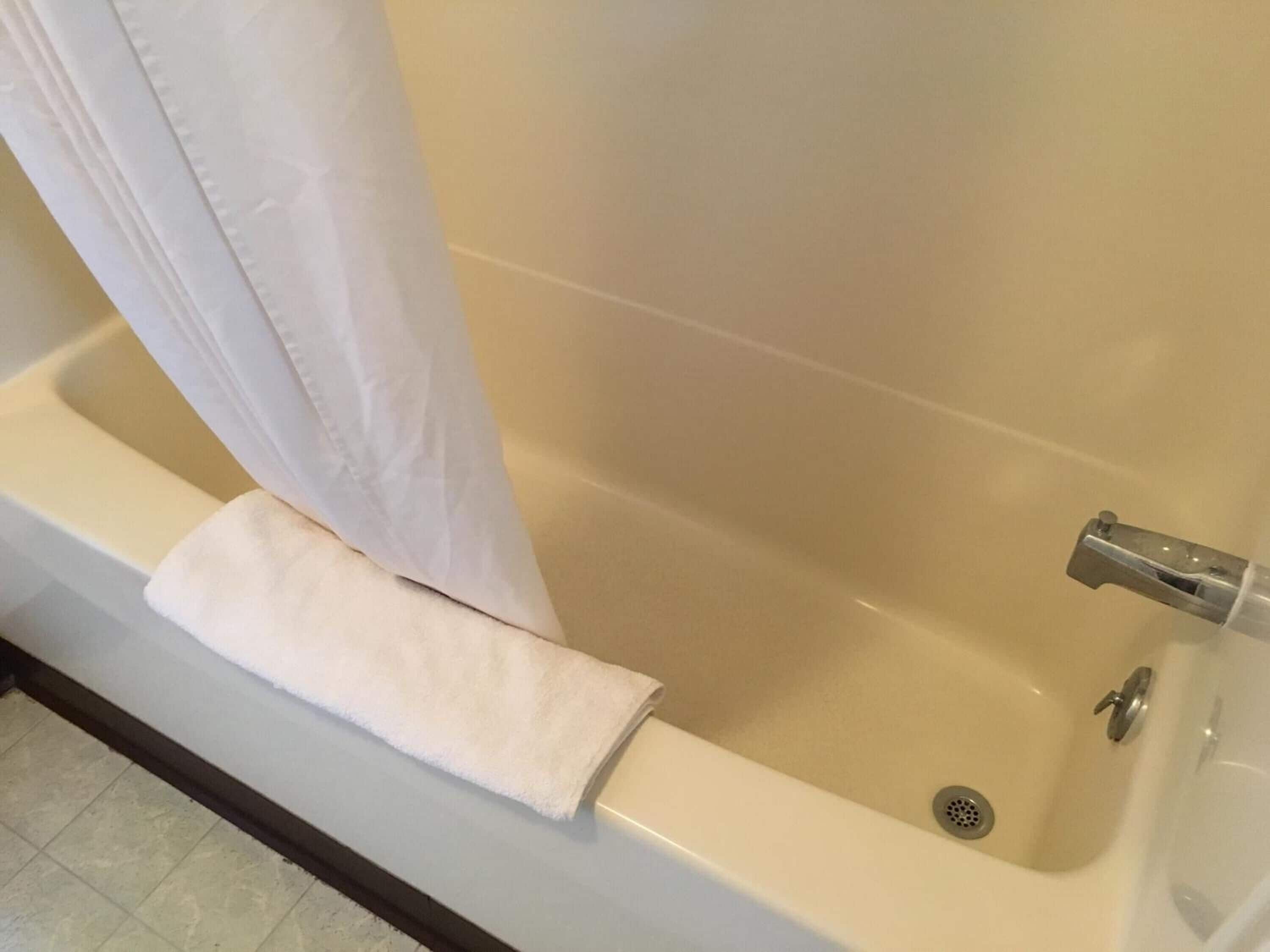 Una bañera con una toalla blanca y una cortina de ducha.