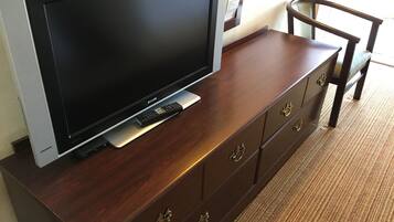 Un televisor de pantalla plana sobre un mueble de madera, con un control remoto, una silla y una puerta al fondo.