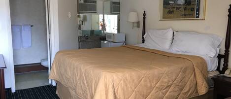 Habitación de hotel con una cama grande, baño con inodoro y lavamanos, un espejo y un cuadro enmarcado en la pared.