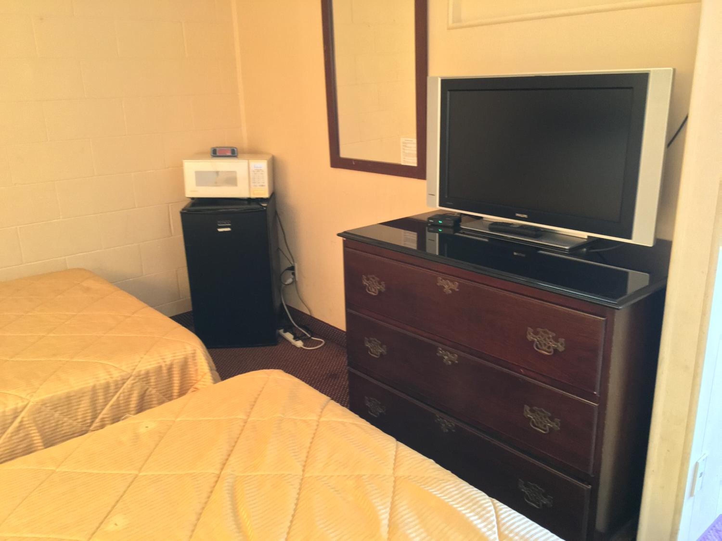 Une petite chambre d’hôtel avec deux lits, une commode équipée d’un téléviseur, un four à micro-ondes et un réfrigérateur.