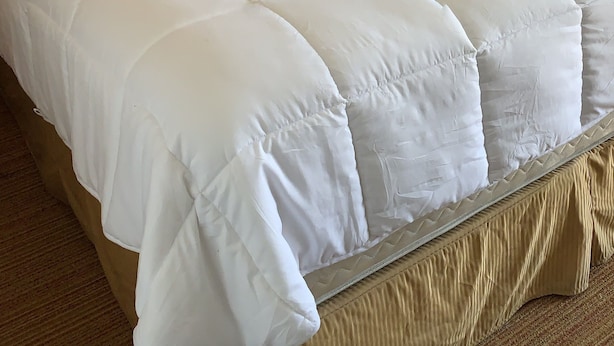 Una cama grande con edredón blanco acolchado, cabecera de madera y lámpara de noche.