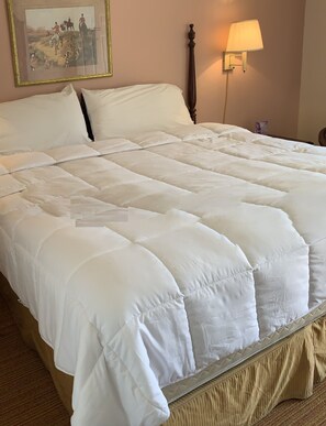 Una cama grande con edredón blanco acolchado, cabecera de madera y lámpara de noche.