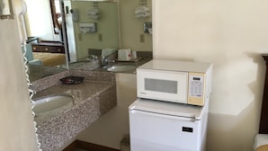 Una cocina compacta con encimeras de granito, un microondas blanco y un refrigerador pequeño.